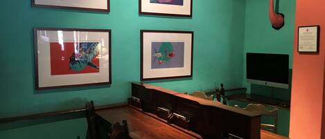 A room with teal walls, a wooden desk, and four framed artworks.