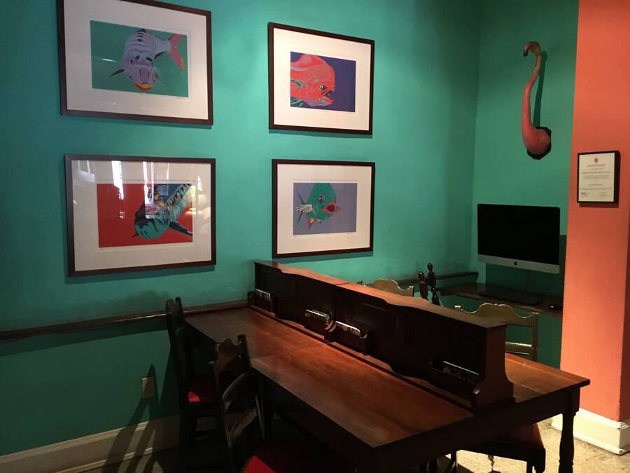 Ein Zimmer mit türkisfarbenen Wänden, einem Holztisch und vier gerahmten Kunstwerken.