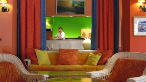 A lobby with a green wall, a reception desk, a sofa with patterned cushions, and wicker chairs. - Colony Hotel & Cabaña Club (Delray Beach)