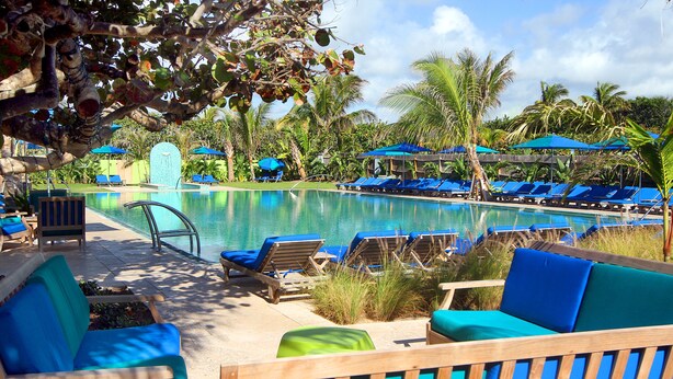 A poolside area with lounge chairs and umbrellas, surrounded by palm trees and a clear sky. - Colony Hotel & Cabaña Club (Delray Beach)