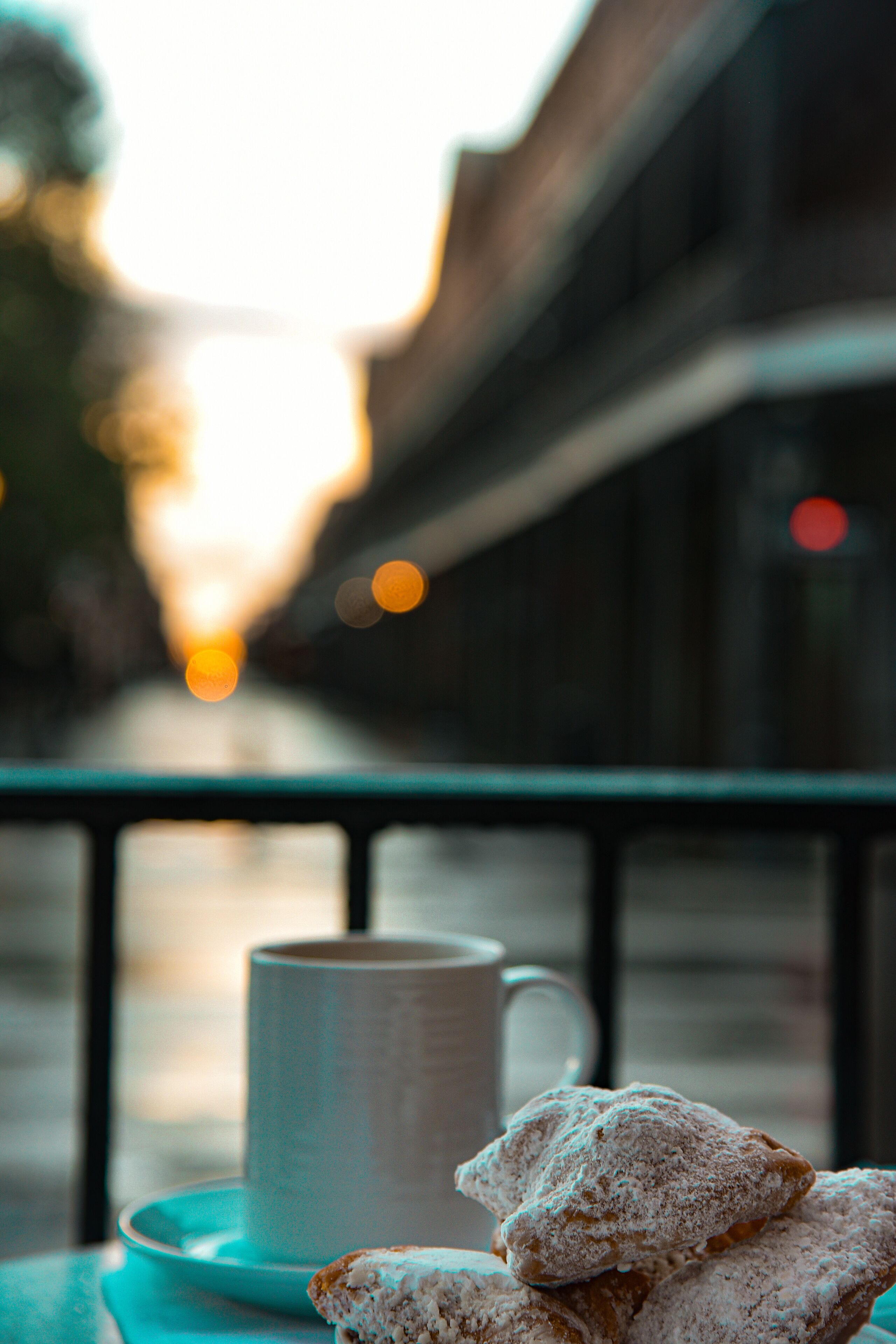 A table with a cup and pastries, a railing, and a blurred street view in the background.