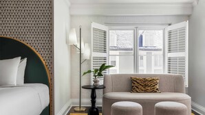 Habitación de hotel con cama, sofá, una mesita con una planta y una lámpara de pie.