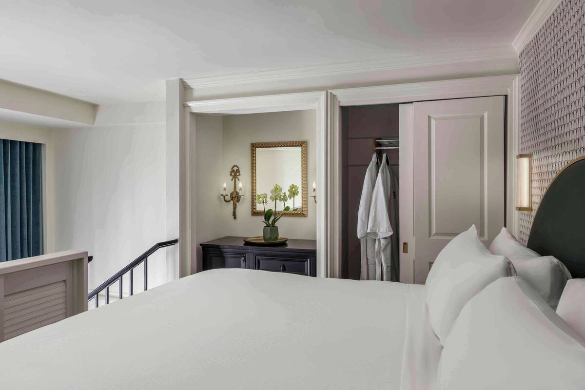 Een hotelkamer met een groot bed, een kaptafel, een spiegel en een deur naar een andere kamer.