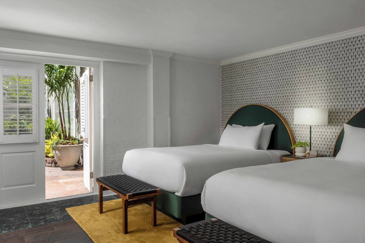 Een hotelkamer met twee bedden, een kleine tafel, een nachtkastje met lamp en uitzicht op de omliggende tuin.