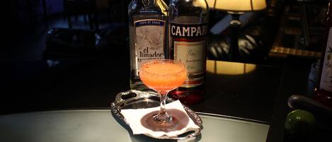 Eine Bar mit einem Cocktailglas auf einer Serviertafel, zwei alkoholischen Getränken und einer Lampe im Hintergrund.