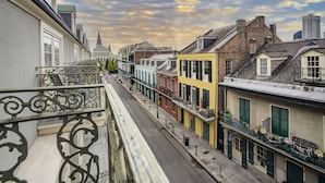 Una hilera de edificios históricos con balcones, cielo despejado y la aguja de una iglesia a lo lejos.