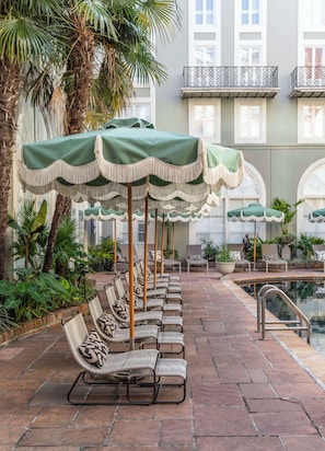 A row of wicker lounge chairs with green umbrellas, a pool, and a building with balconies in the background. - Bourbon Orleans Hotel (New Orleans)