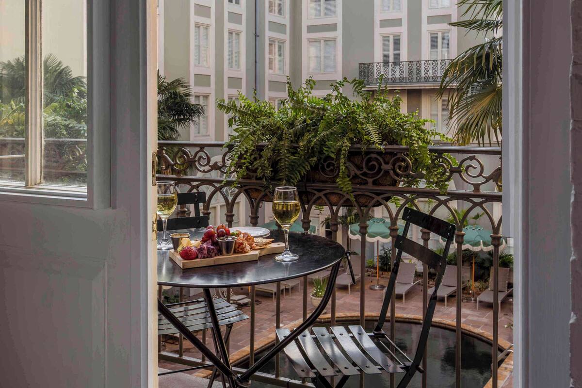 Een balkon met een eettafel, omringd door stoelen, met uitzicht op een binnenplaats vol gebouwen en groen.