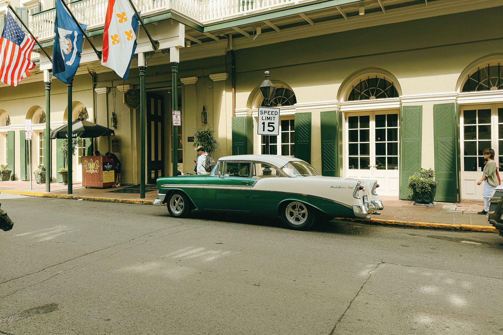 A vintage green and white car parked in front of a building with a speed limit sign of 15 mph.