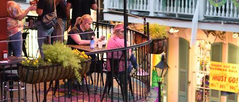 A bustling street scene with outdoor seating on a balcony, a stop sign, and a one-way sign.