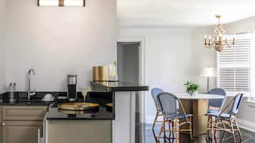 Cozinha moderna com bancada preta, máquina de café e área de refeições com cadeiras de vime e uma mesa pequena.