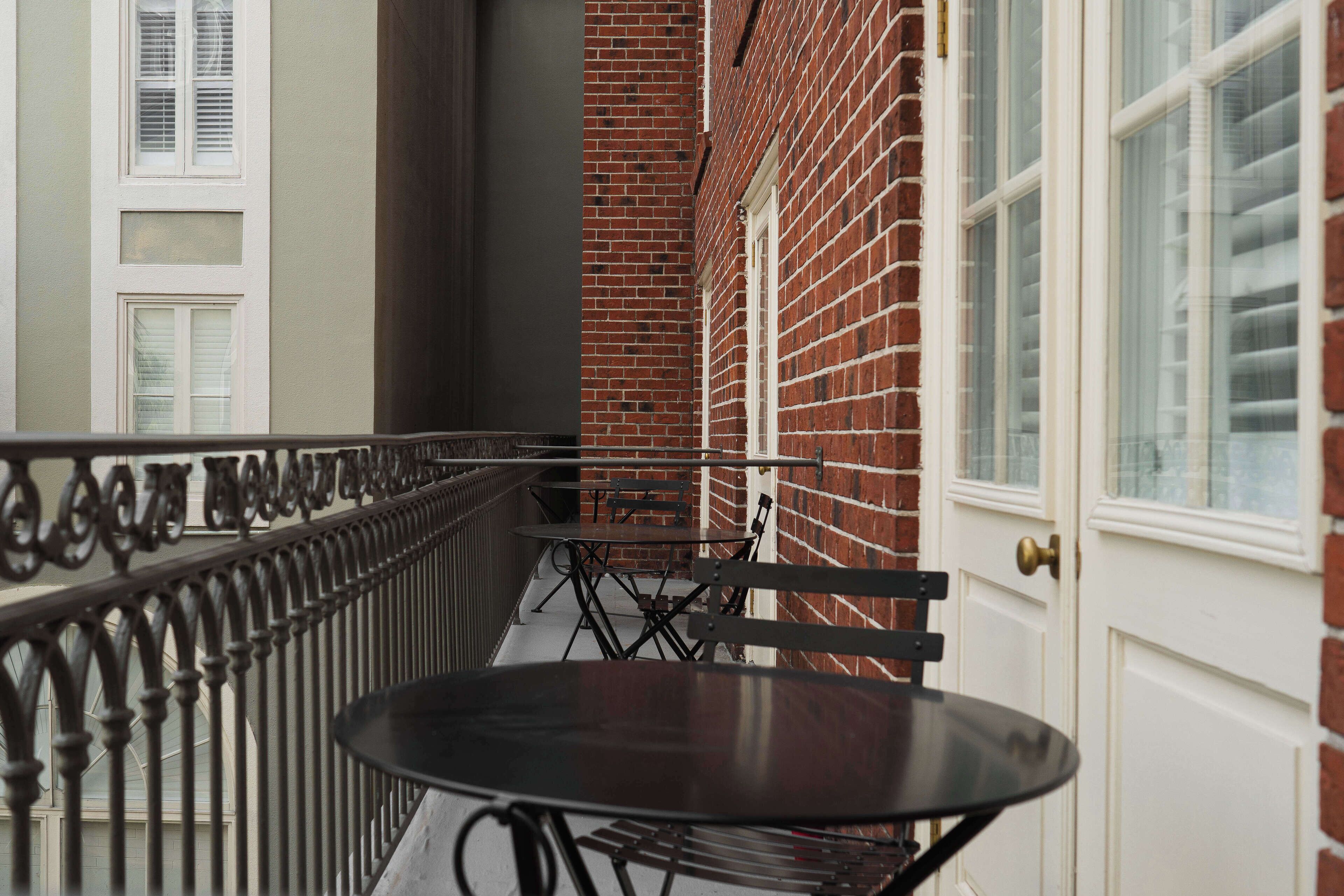 A narrow outdoor corridor with a brick wall, a white door, and a metal railing.