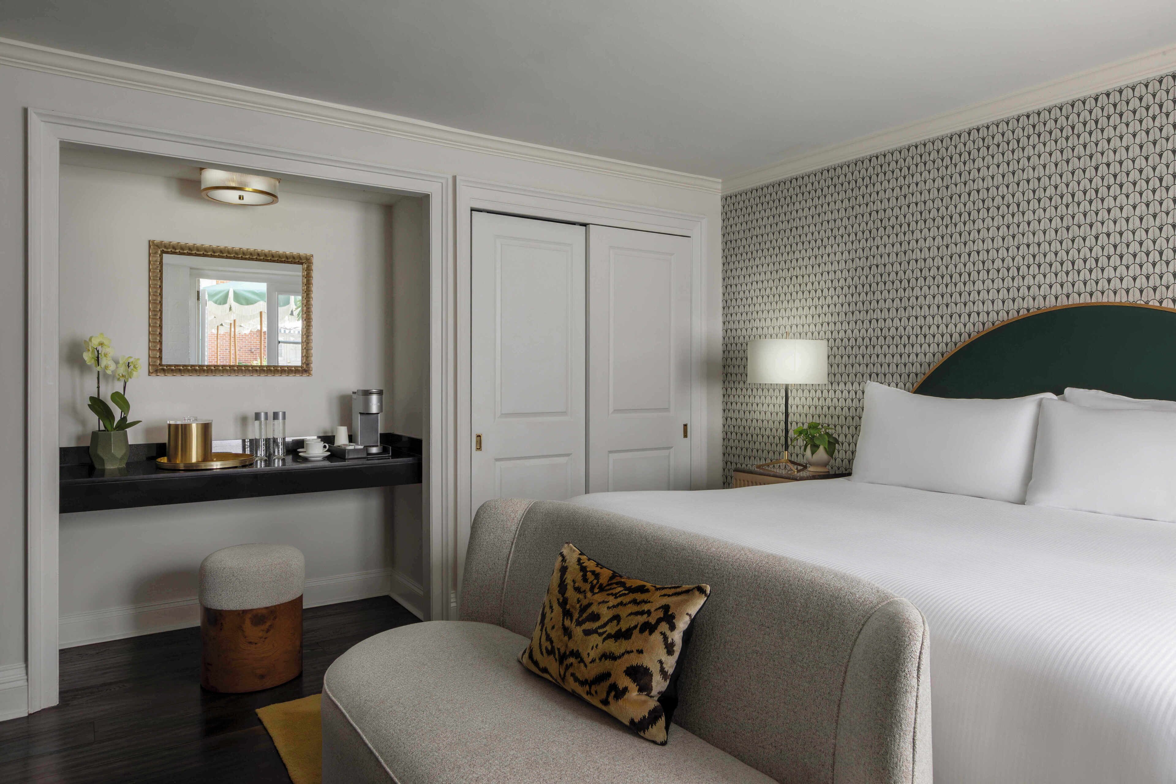 Une chambre d’hôtel avec un lit, un canapé, une petite table avec une lampe, un miroir et un mur décoré d’un motif.