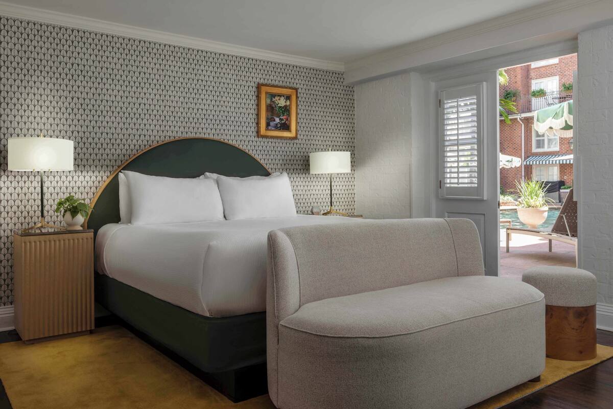 Een keurig opgemaakt slaapkamer met een bed, twee bedlampen, een groen hoofdeinde en uitzicht op het balkon.