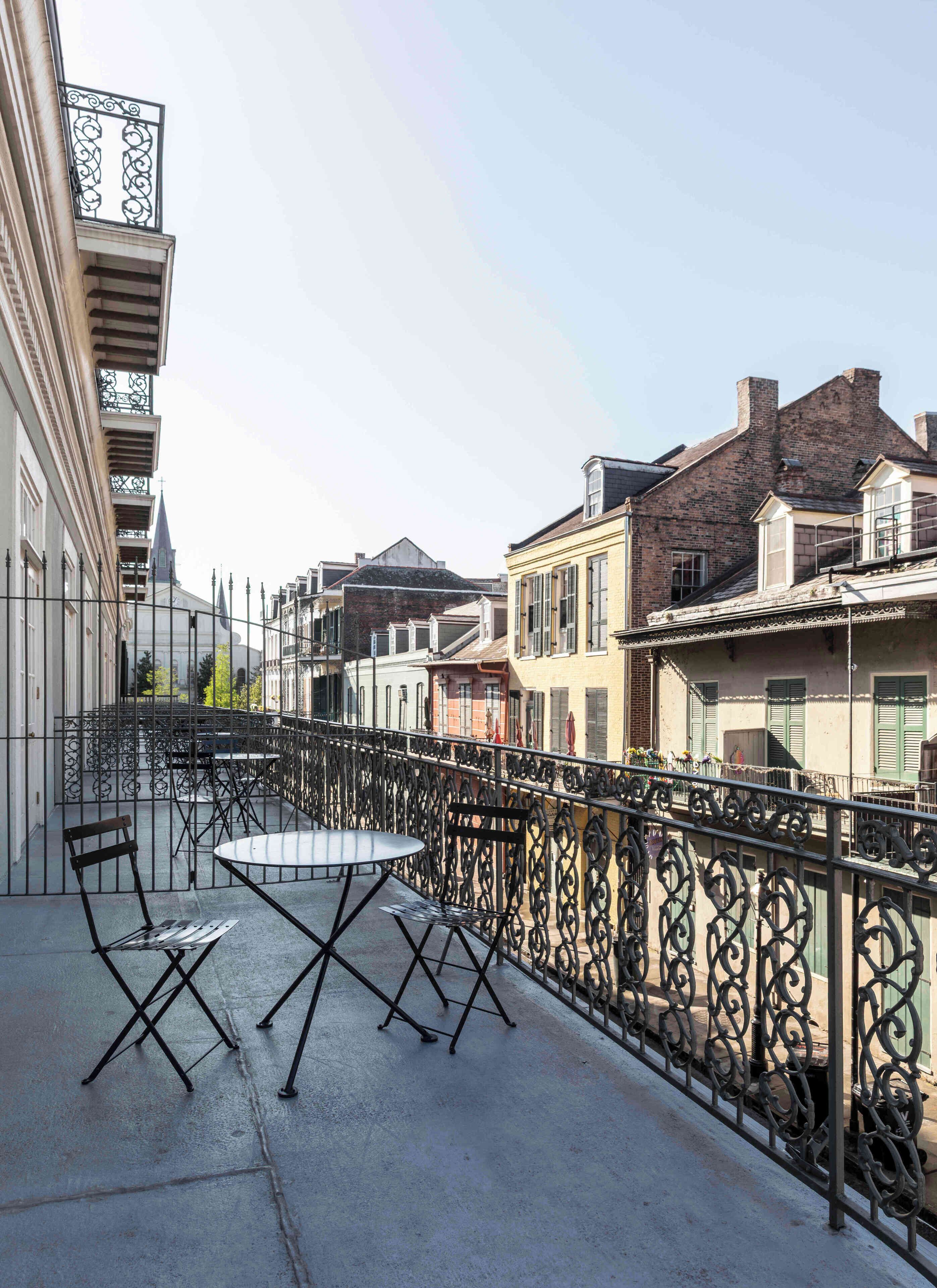 Een balkon met een ronde tafel en stoelen, omgeven door gedecoreerd zwart metalen hekwerk.