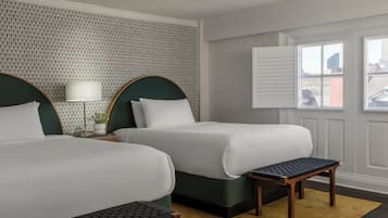 Habitación de hotel con dos camas, una mesita, un banco y una ventana con persianas.