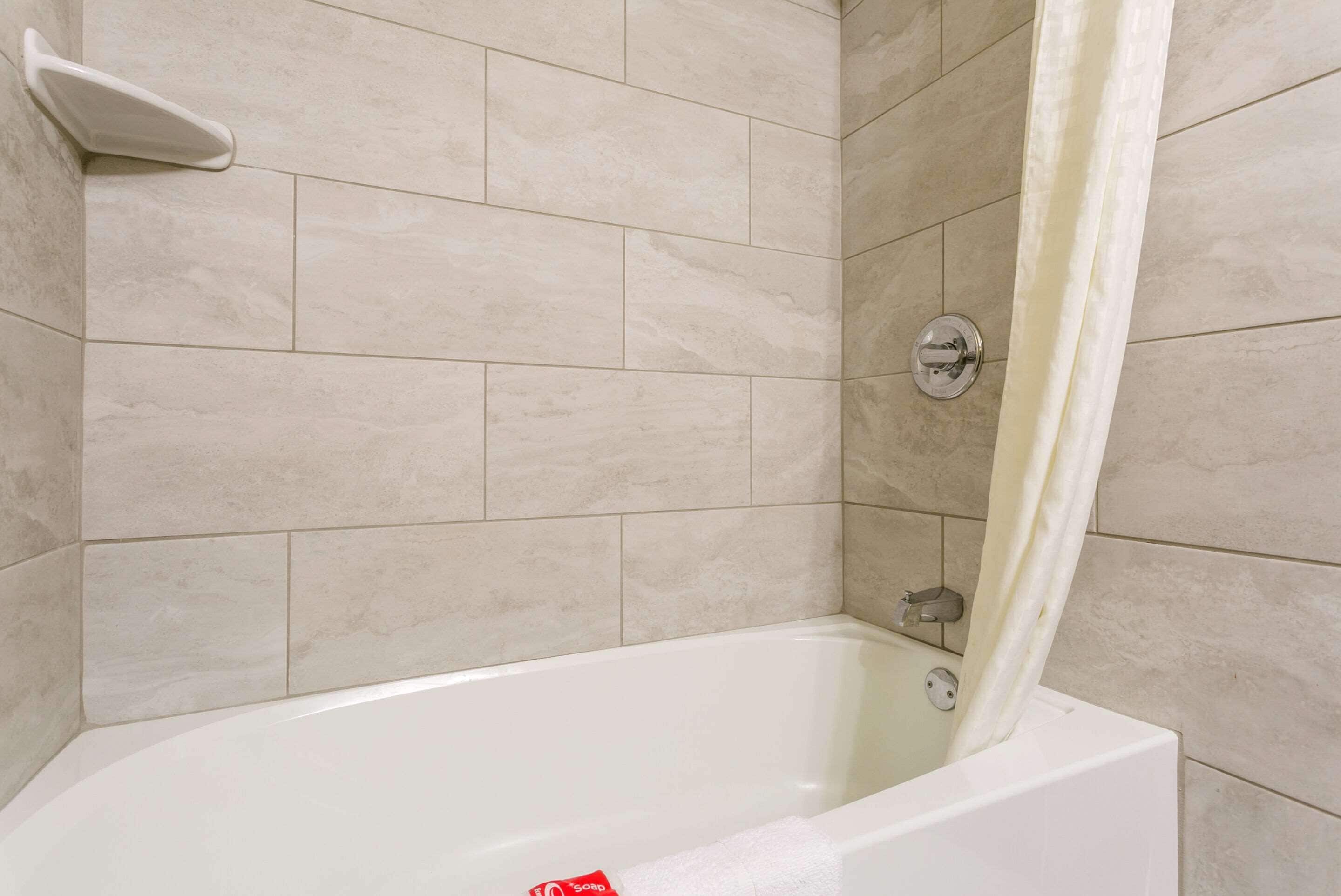 Un baño con bañera, paredes de azulejos, una cortina de ducha y un dispensador de jabón.