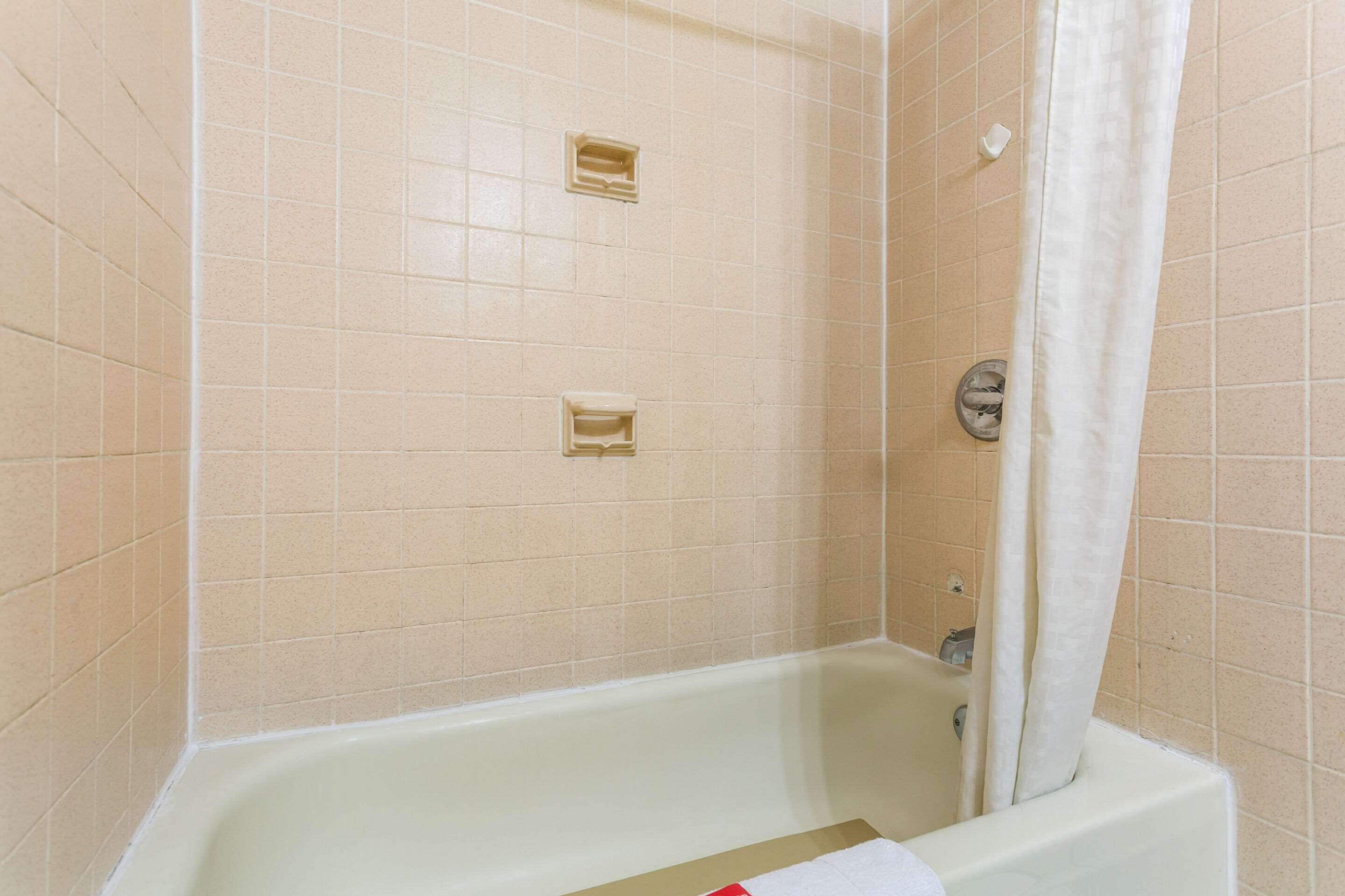 Un baño con paredes de azulejos color beige, una bañera blanca y una cortina de ducha.