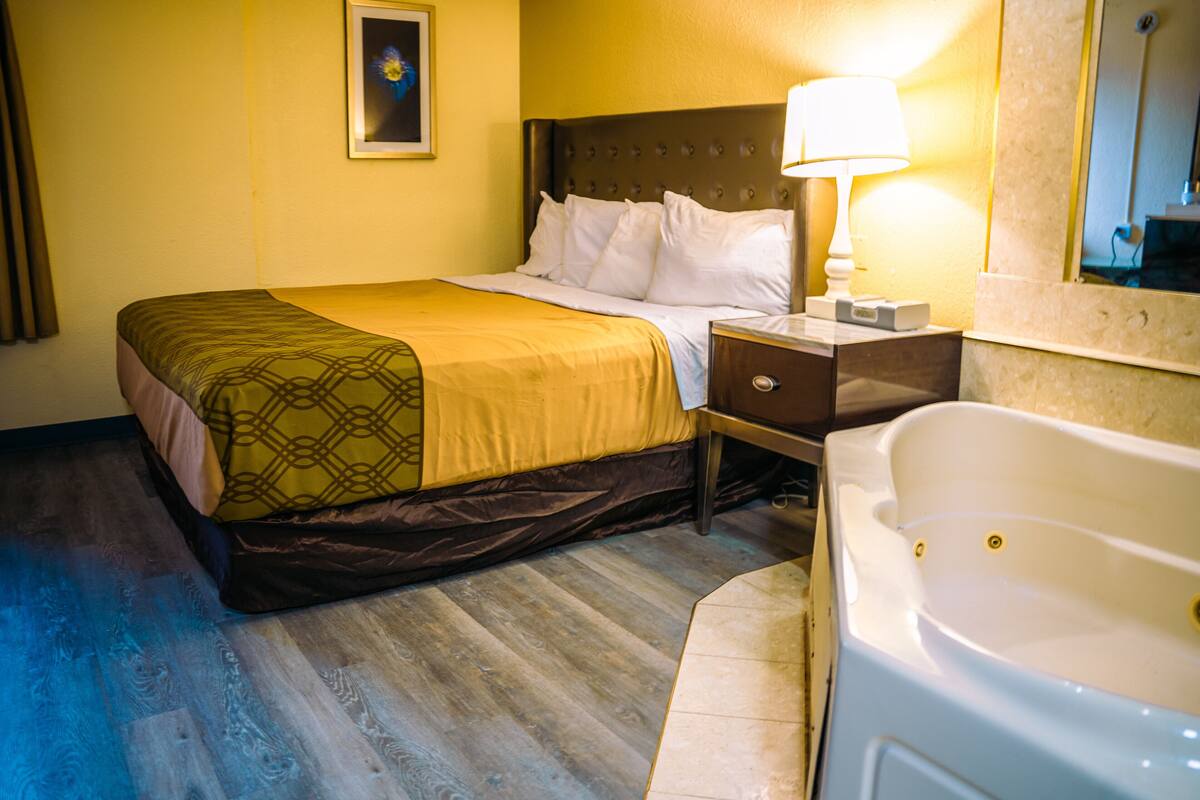 A hotel room with a bed, bedside table, lamp, and a bathtub.