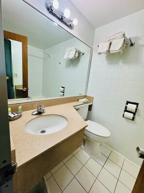 A bathroom with a sink, mirror, towel rack, toilet, and a towel dispenser.