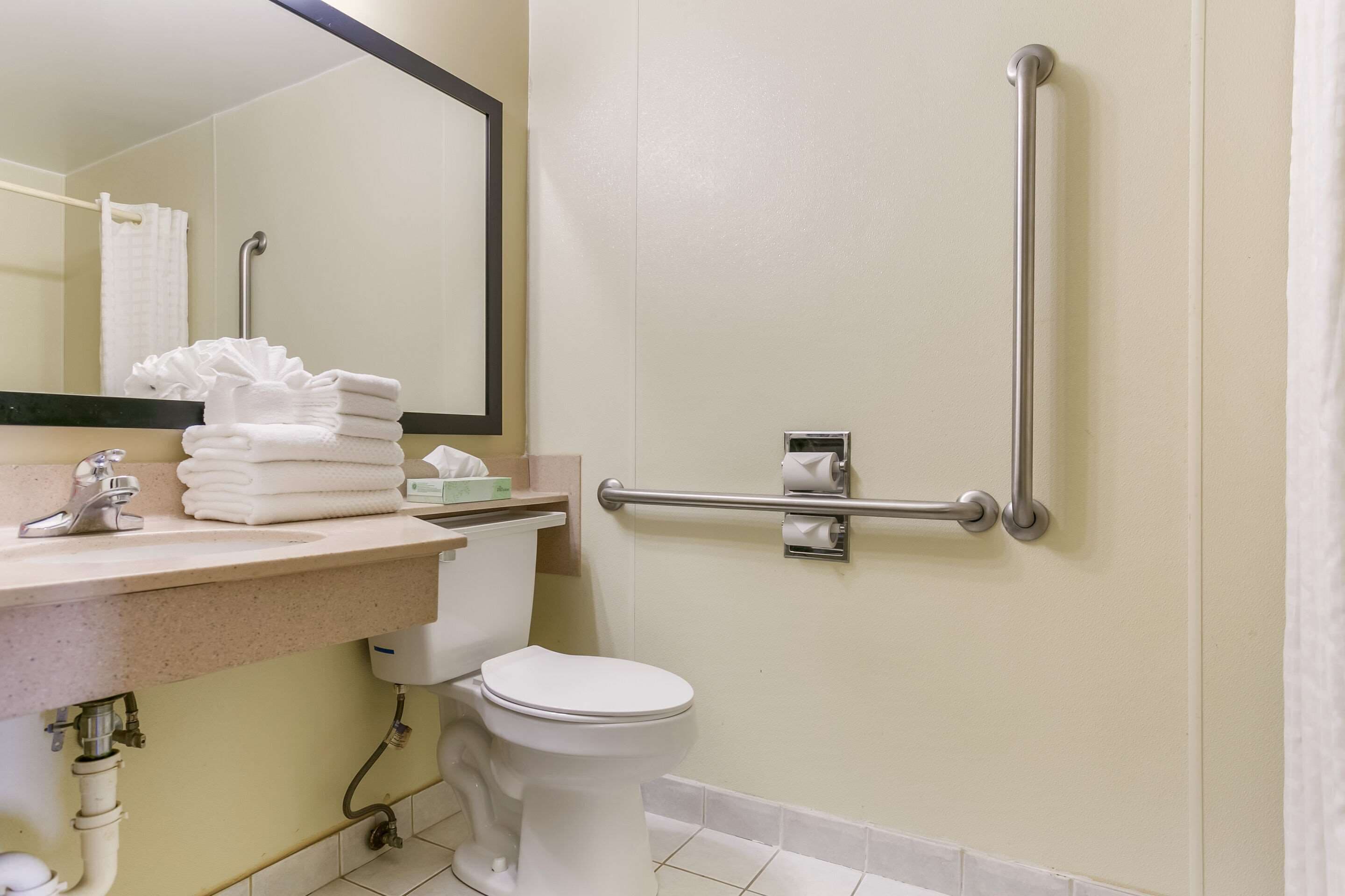 Un baño con inodoro, lavamanos y barra de apoyo para accesibilidad.