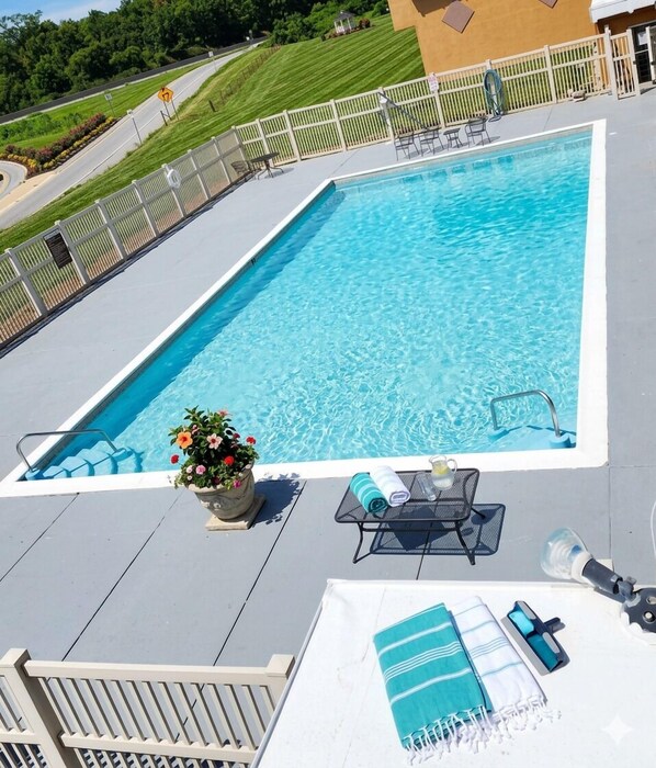 A rectangular swimming pool with a surrounding deck, a potted plant, and outdoor furniture.