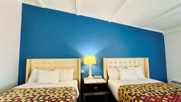 A hotel room with two beds, each with a patterned bedspread, a bedside table with a lamp, and a wall painted blue.