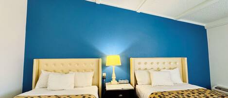 A hotel room with two beds, each with a patterned bedspread, a bedside table with a lamp, and a wall painted blue.