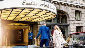 La entrada del Hotel Excelsior Ernst, con una fachada clásica de piedra, una entrada imponente y un coche antiguo estacionado afuera.