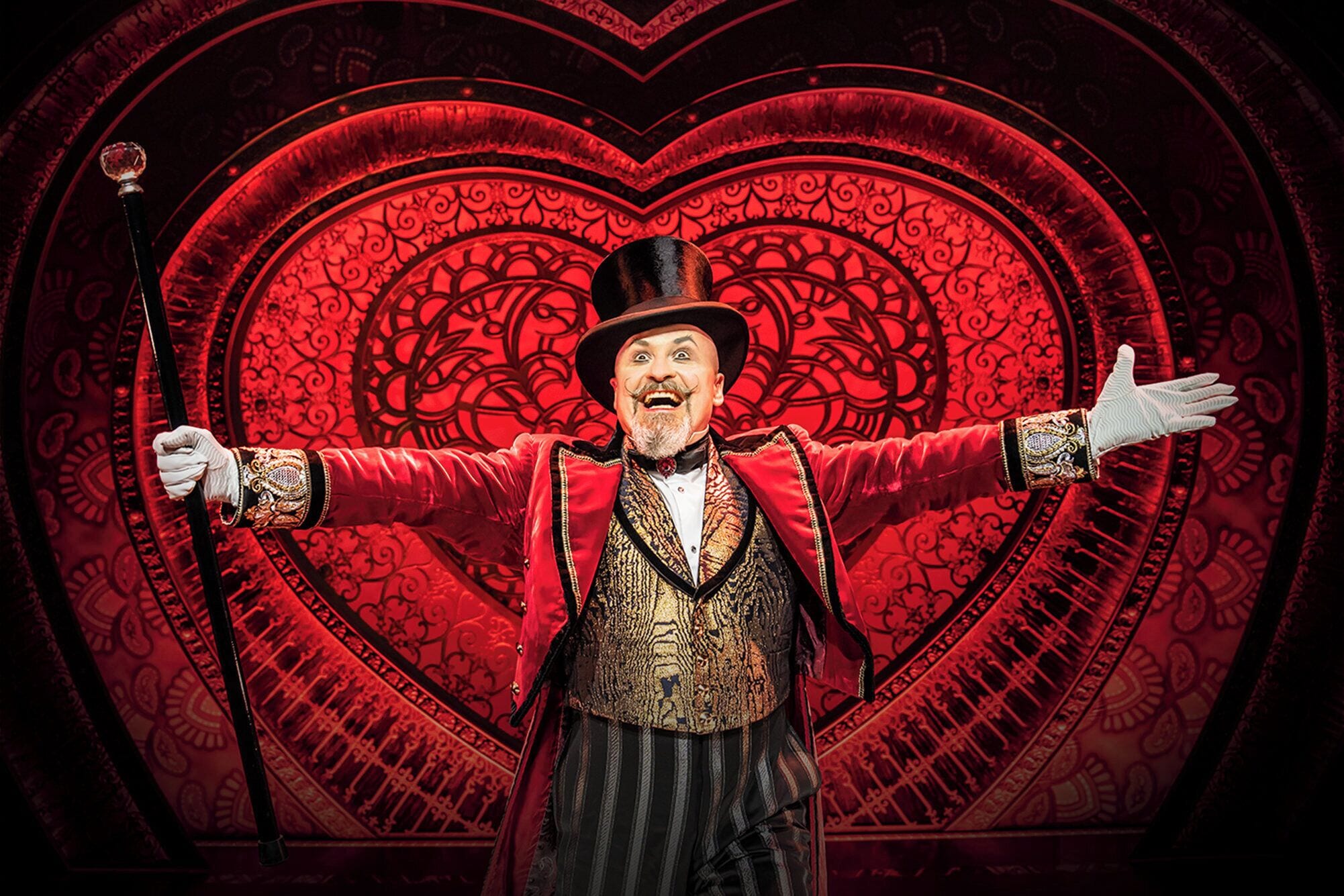 A person in a red jacket and hat standing in front of a large heart-shaped background.