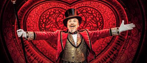 A person in a red jacket and hat standing in front of a large heart-shaped background.