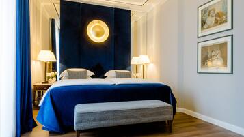 A hotel room with a large bed, two bedside lamps, a bench, and framed artwork on the wall.