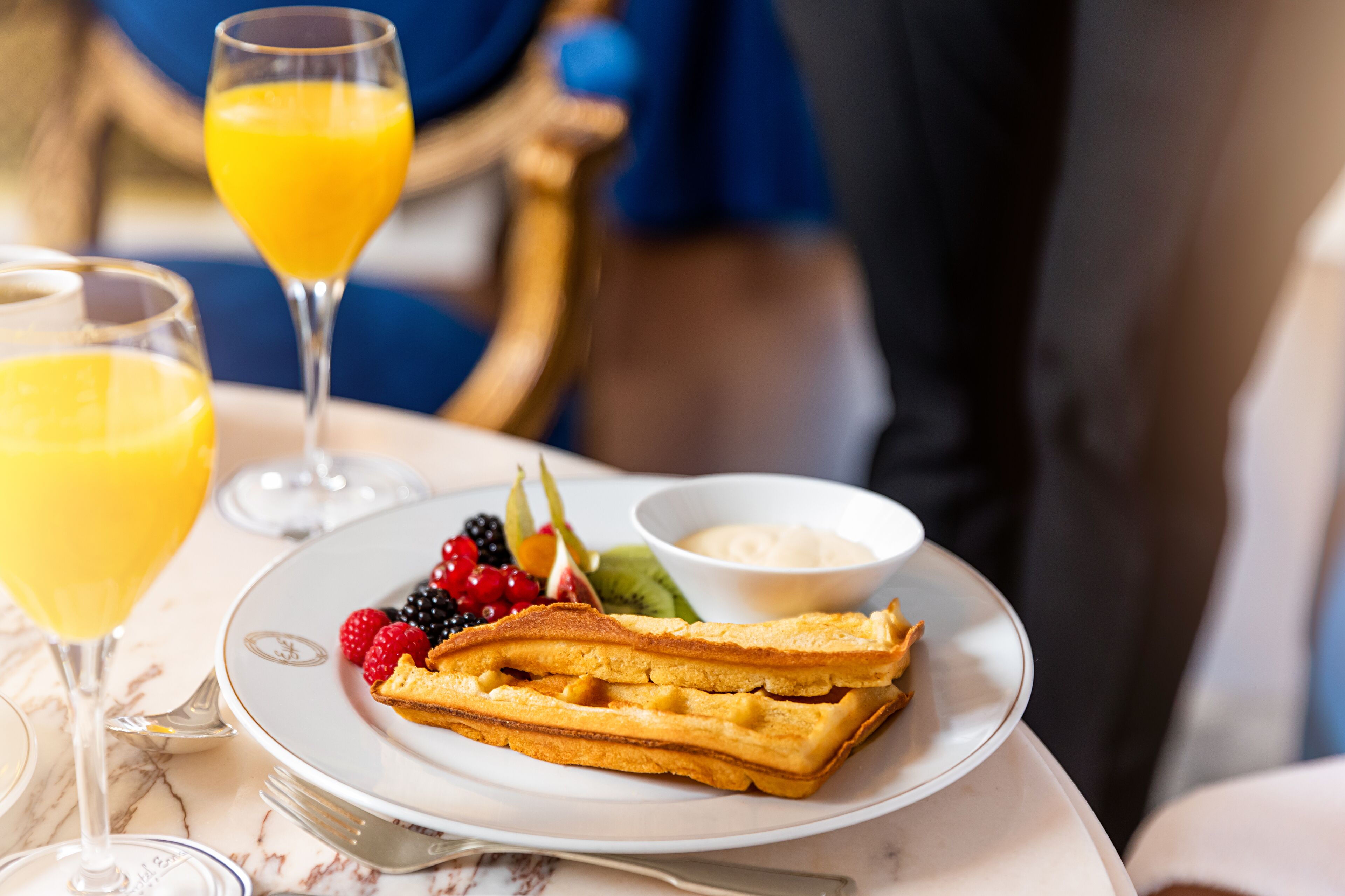 A breakfast setting with waffles, fruit, and a glass of orange juice on a table.