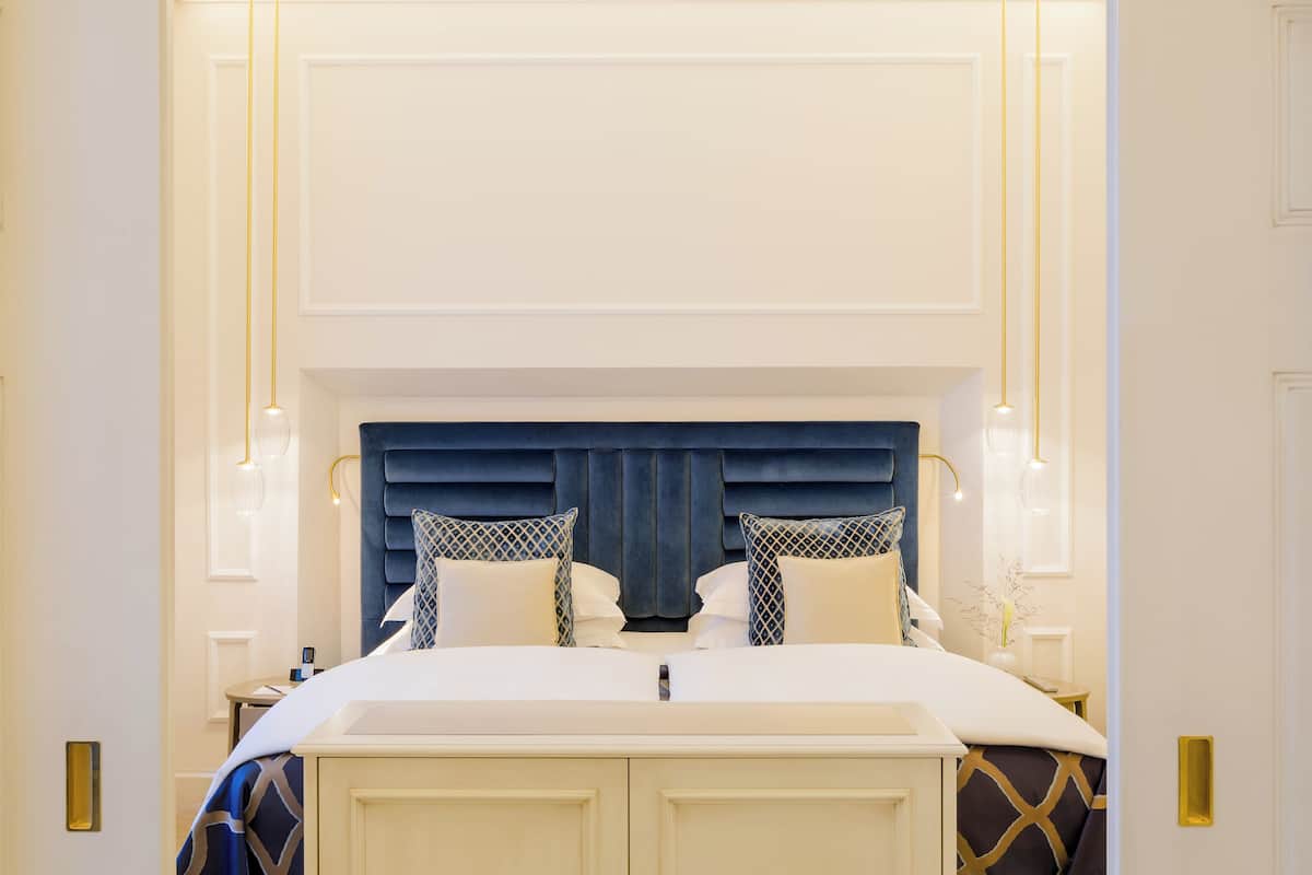 Quarto de hotel moderno com uma cama grande, cabeceira escura e luminárias de cabeceira.
