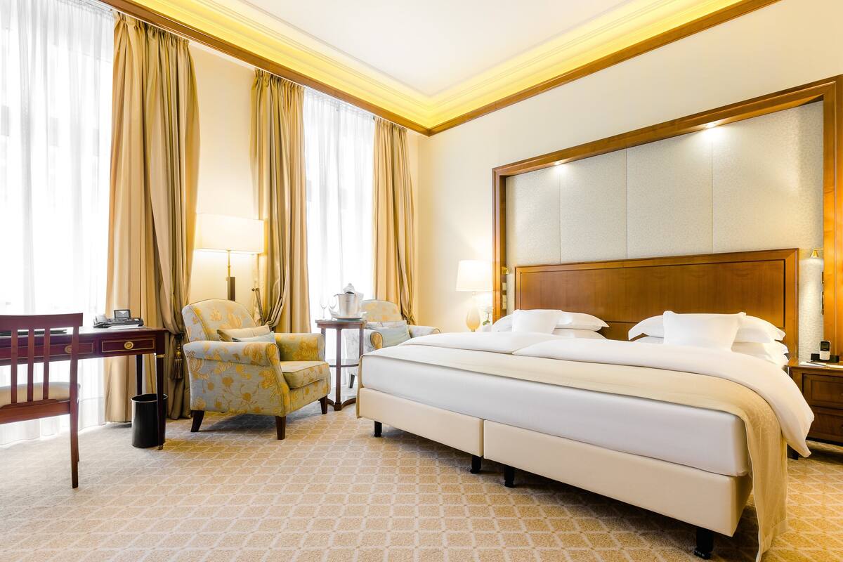Quarto de hotel com uma cama grande, uma escrivaninha, uma cadeira e uma mesinha.