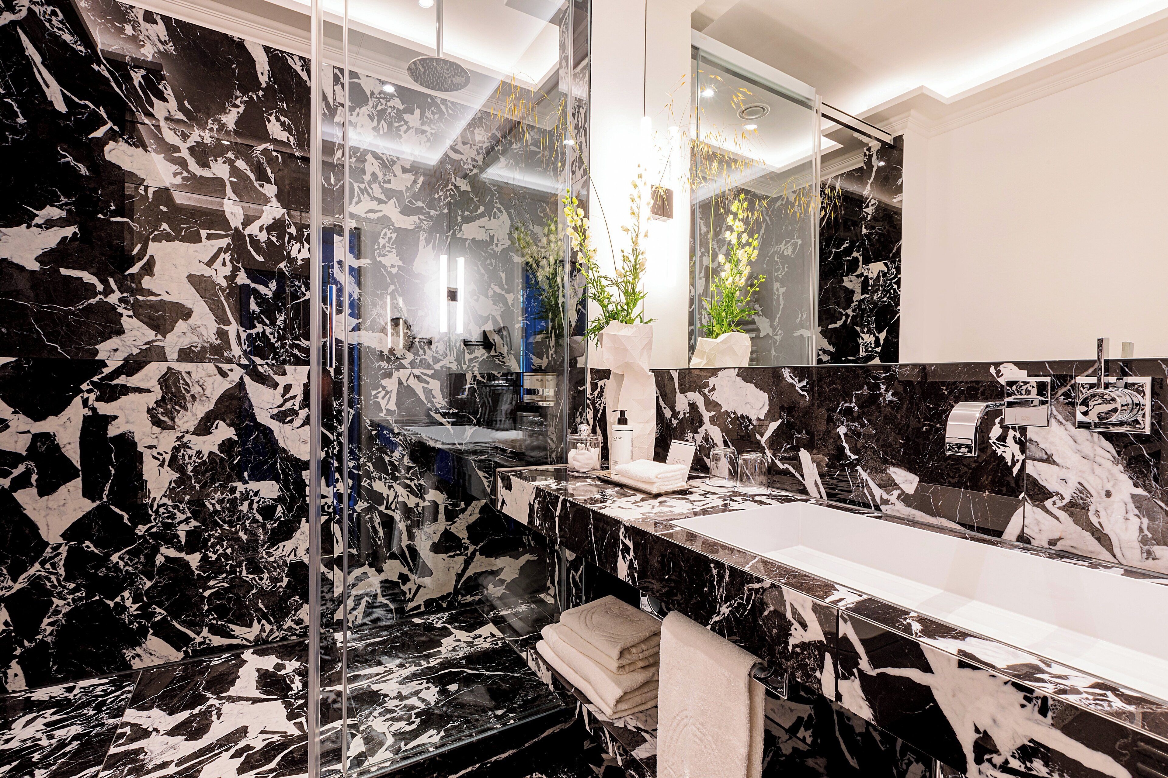 A modern bathroom with a black and white marble countertop, a glass shower enclosure, and a large mirror.