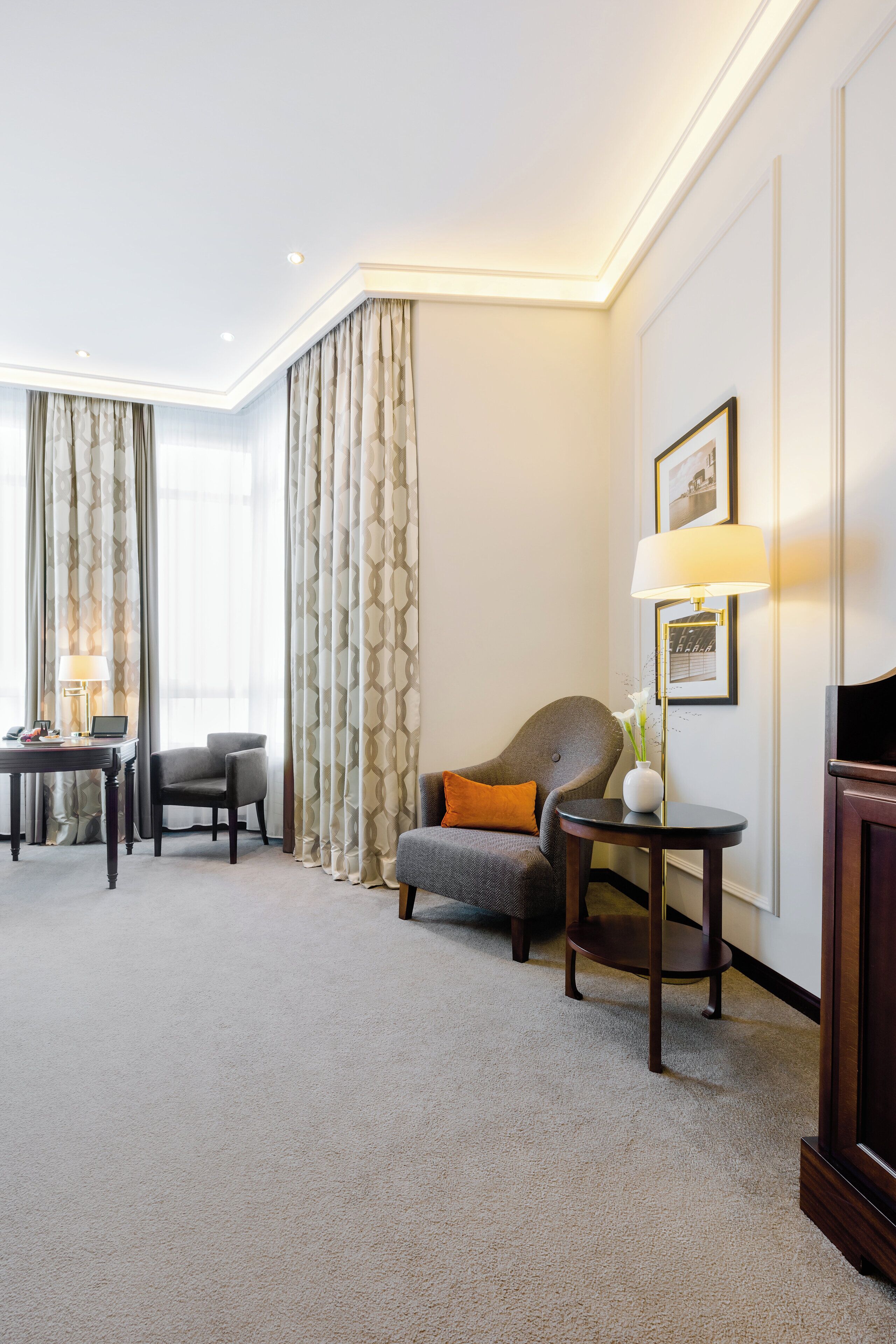 A hotel room with a sofa, armchair, side table, lamp, and a television.