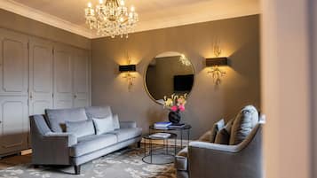 Un salon avec un canapé gris, un miroir rond, un lustre et deux lampes fixées au mur.