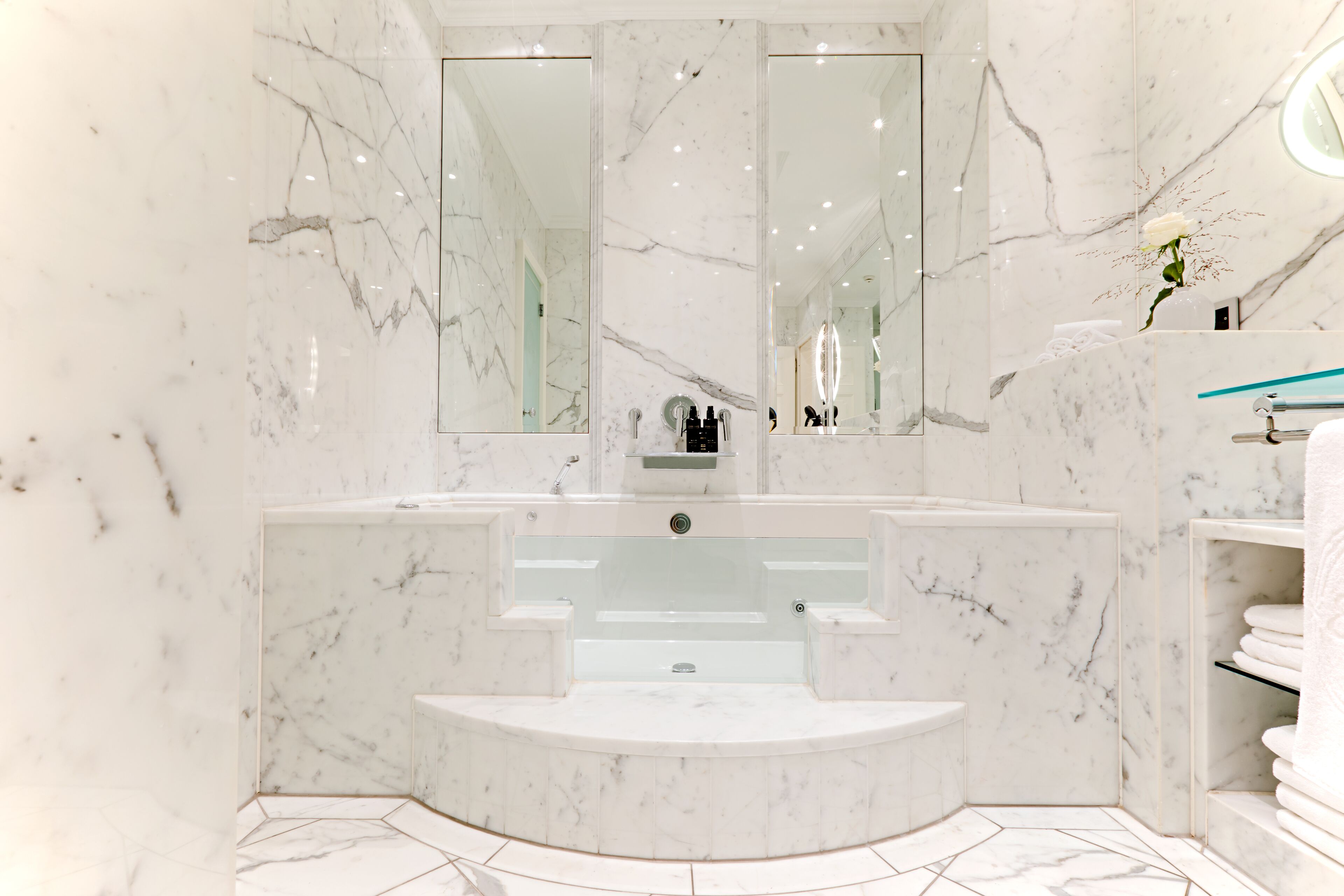 Un baño moderno con tocador de mármol, un espejo grande y una bañera empotrada.