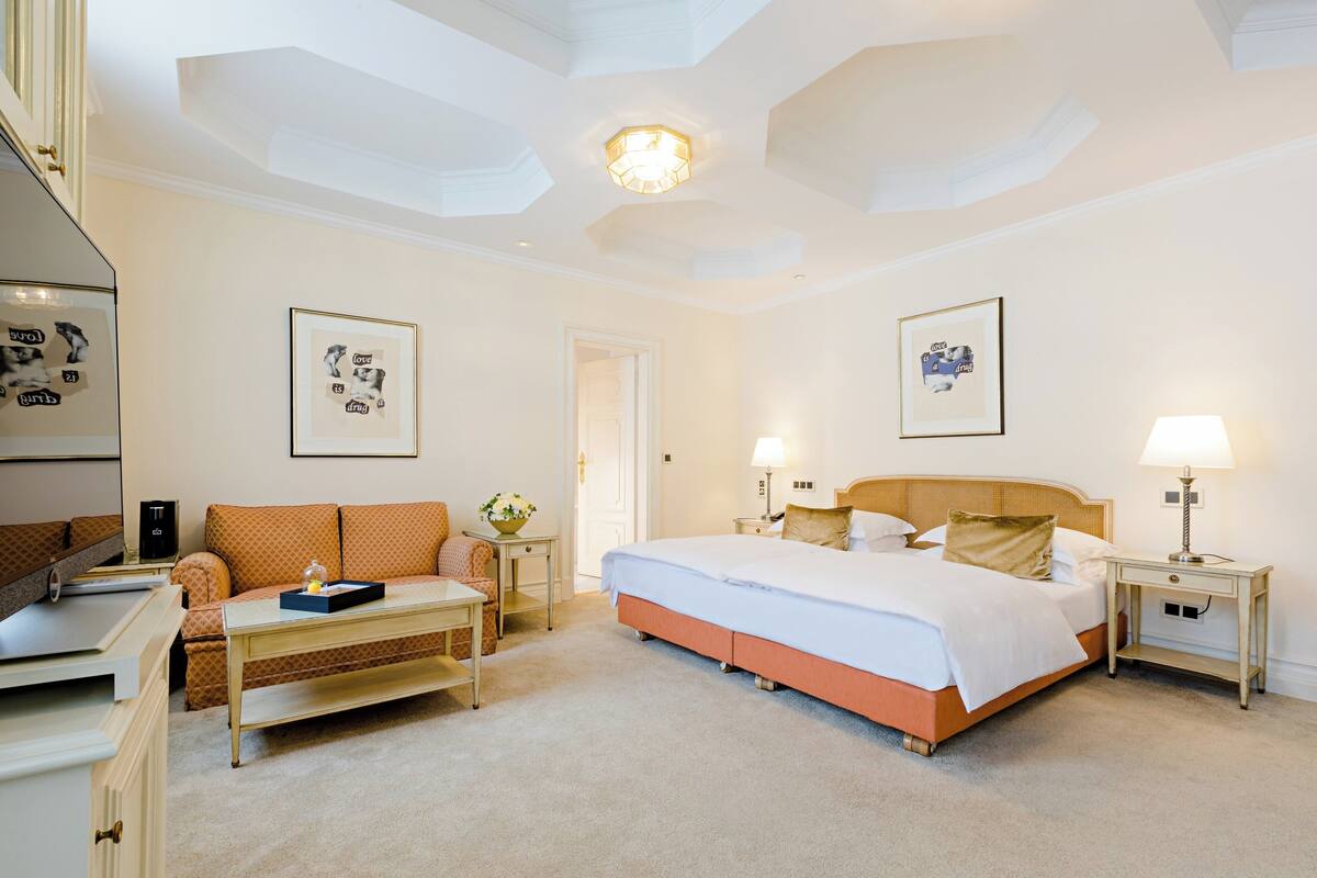 Quarto de hotel com cama, mesas de cabeceira, escrivaninha, cadeira e sofá.