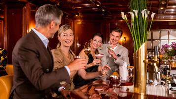 A group of people toasting at a bar with a variety of drinks and a vase of flowers.
