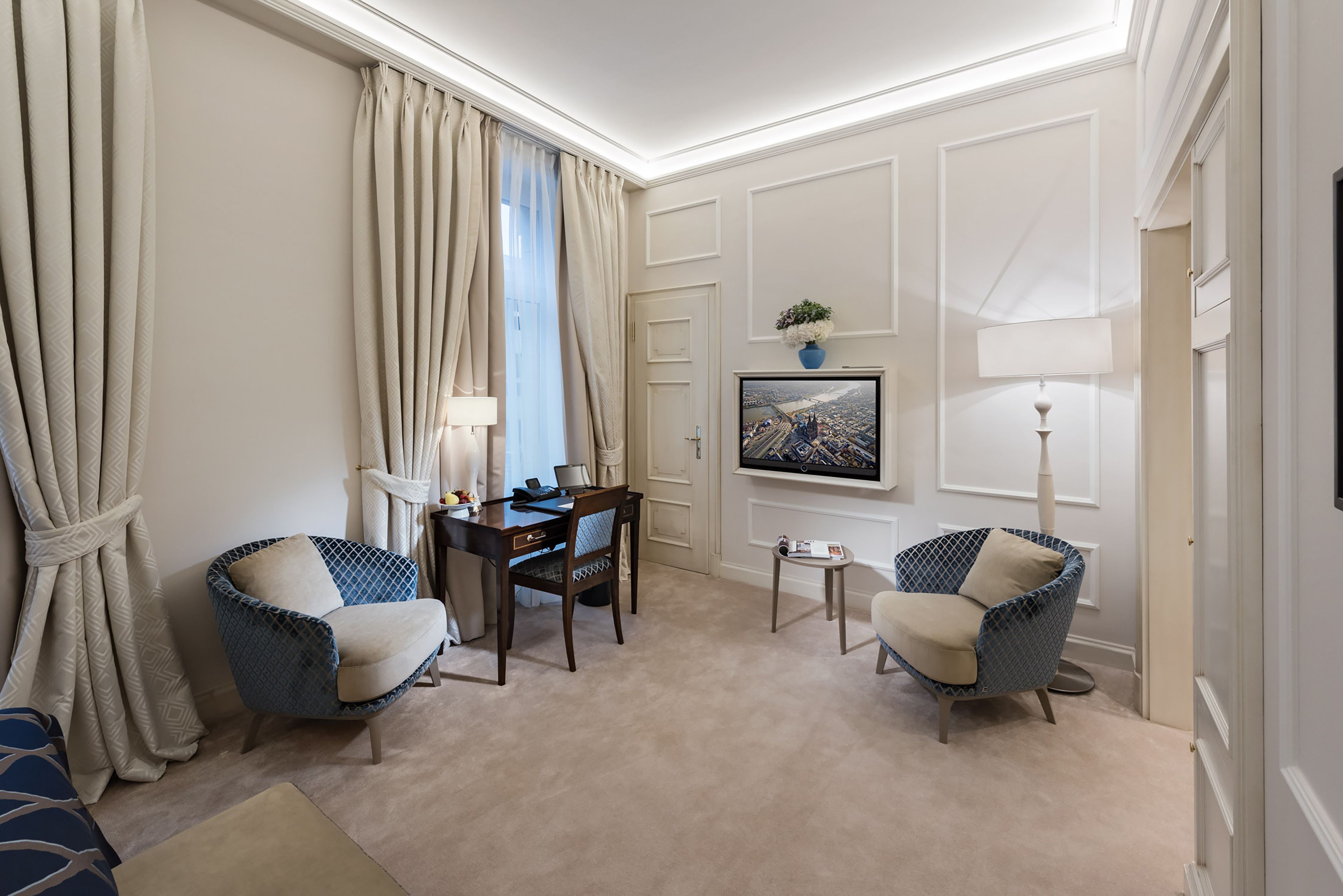 A hotel room with two armchairs, a desk, a television, and a framed picture on the wall.