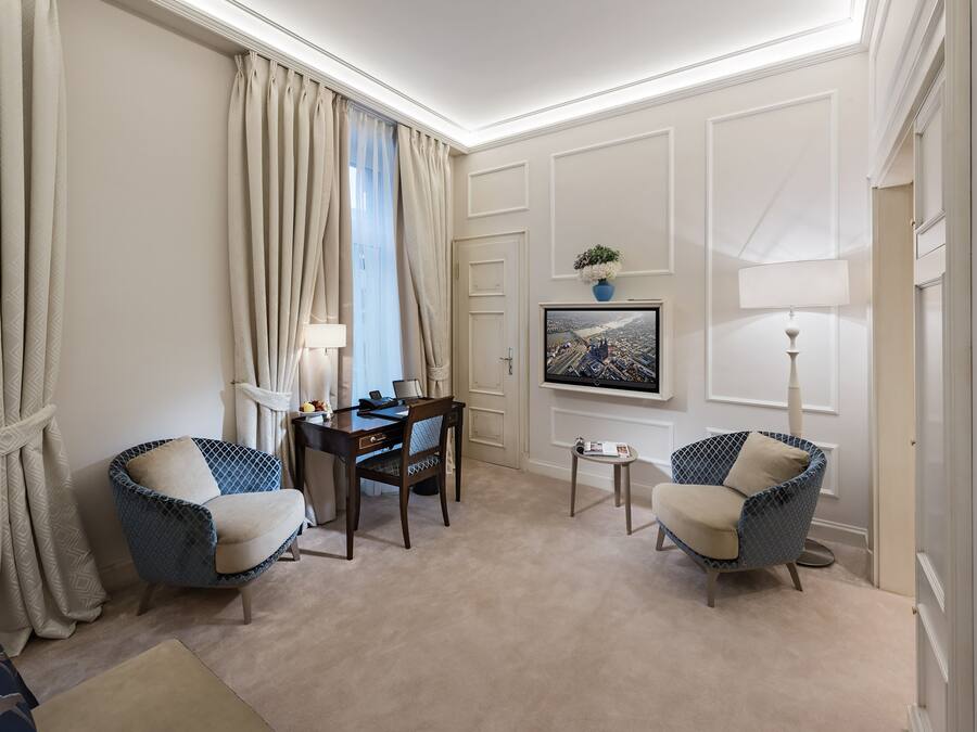 A hotel room with two armchairs, a desk, a television, and a framed picture on the wall.