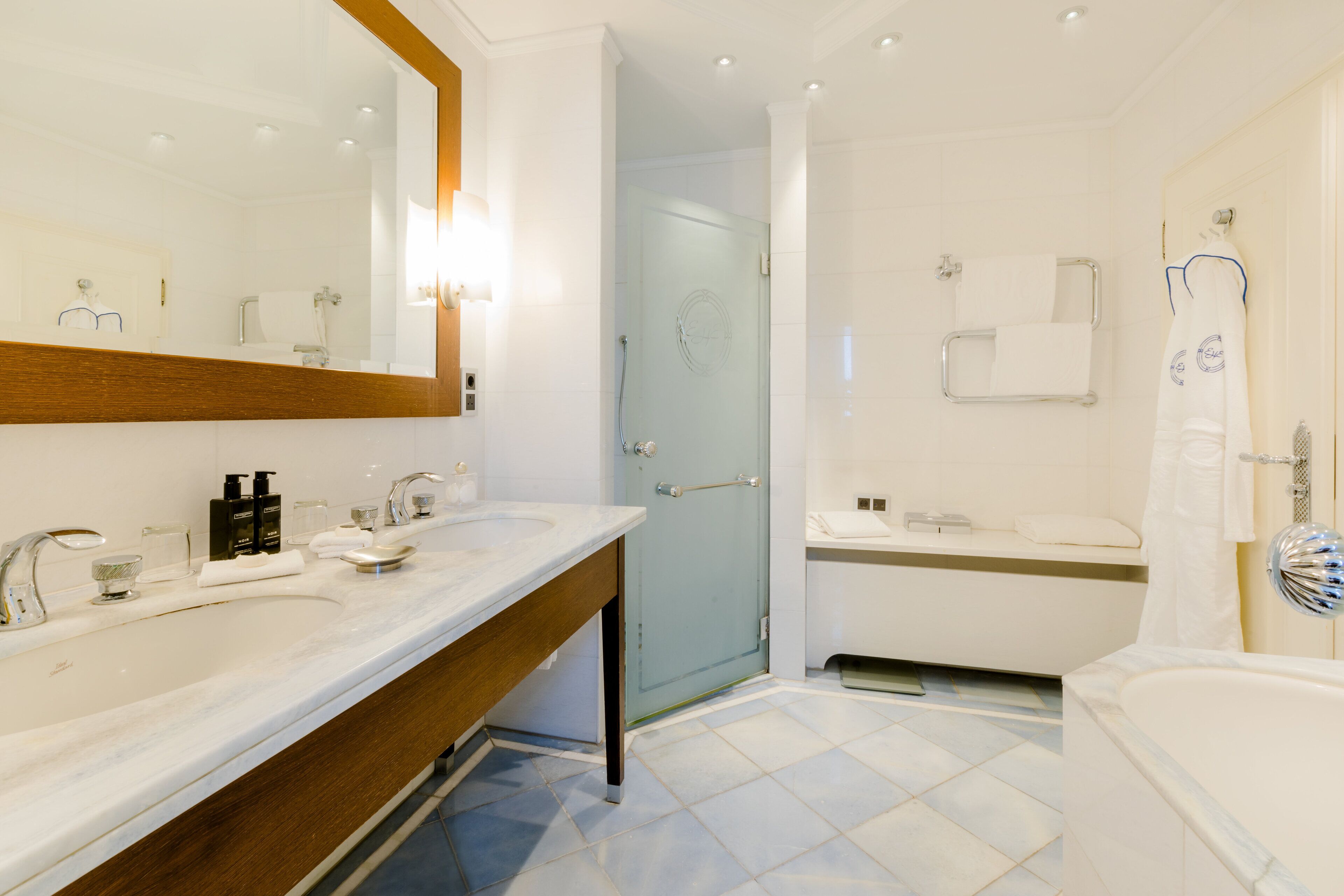 A modern bathroom with two sinks, a large mirror, a glass shower door, and a bathtub.