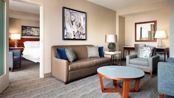 A hotel room with a sofa, armchairs, a coffee table, a bed, and artwork on the walls.