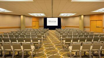 Une salle de conférence avec des rangées de chaises, un grand écran affichant le logo « Westin Hotels & Resorts », et un tapis orné d’un motif géométrique.