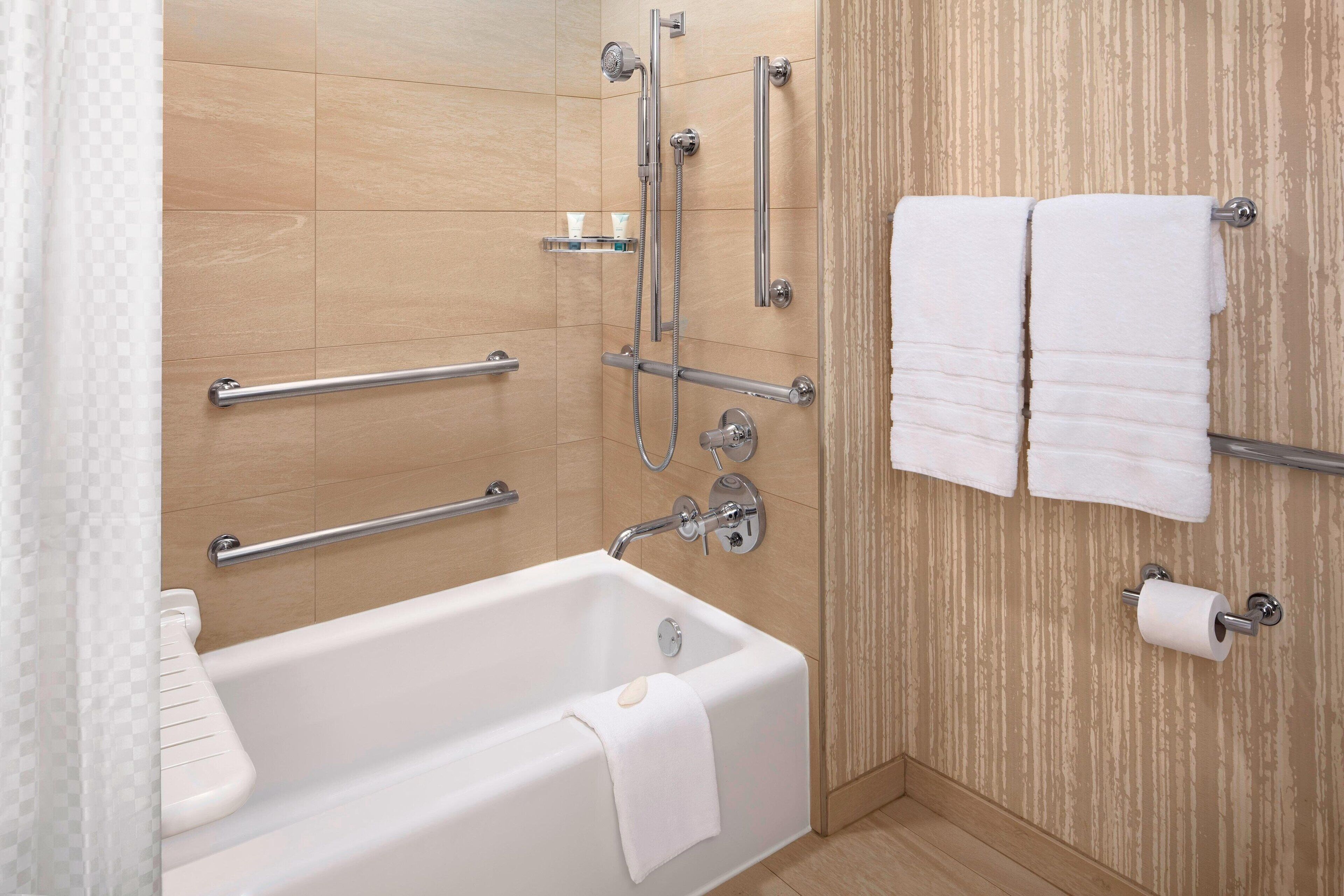 A modern bathroom with a bathtub, grab bars, a showerhead, and towels on a rack.