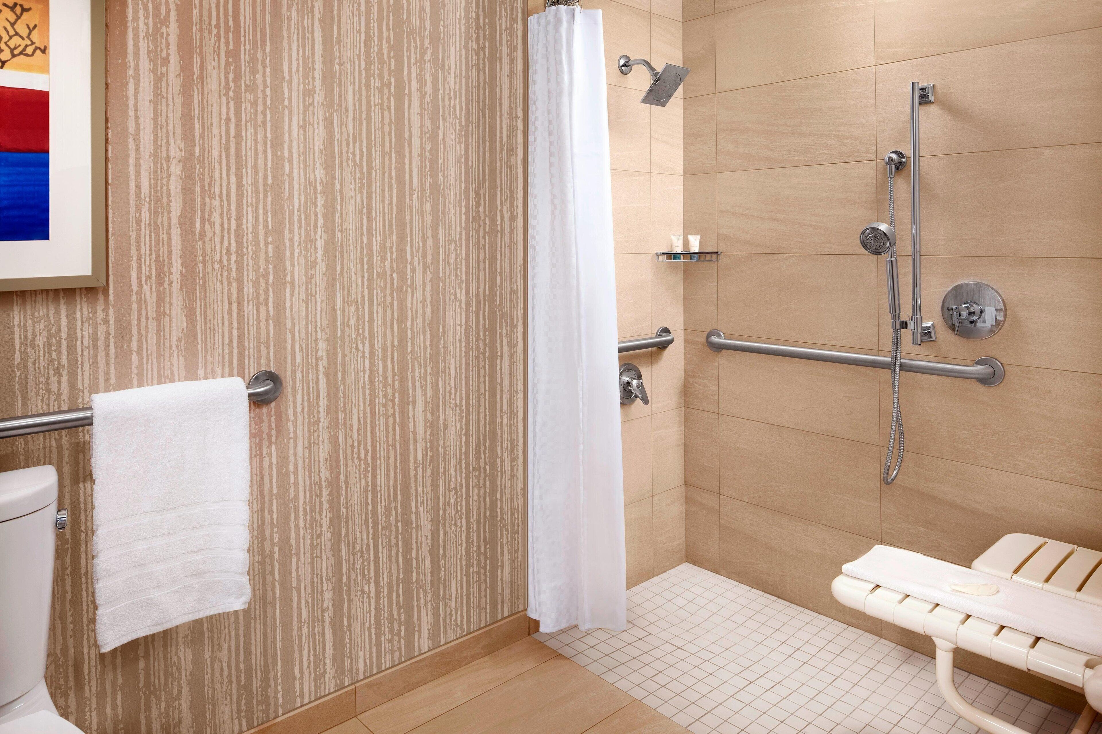 A bathroom with a shower, a toilet, a grab bar, and a bench.