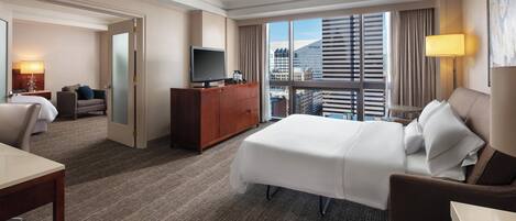 Quarto de hotel com uma cama grande, uma escrivaninha, uma televisão e vista para a cidade.