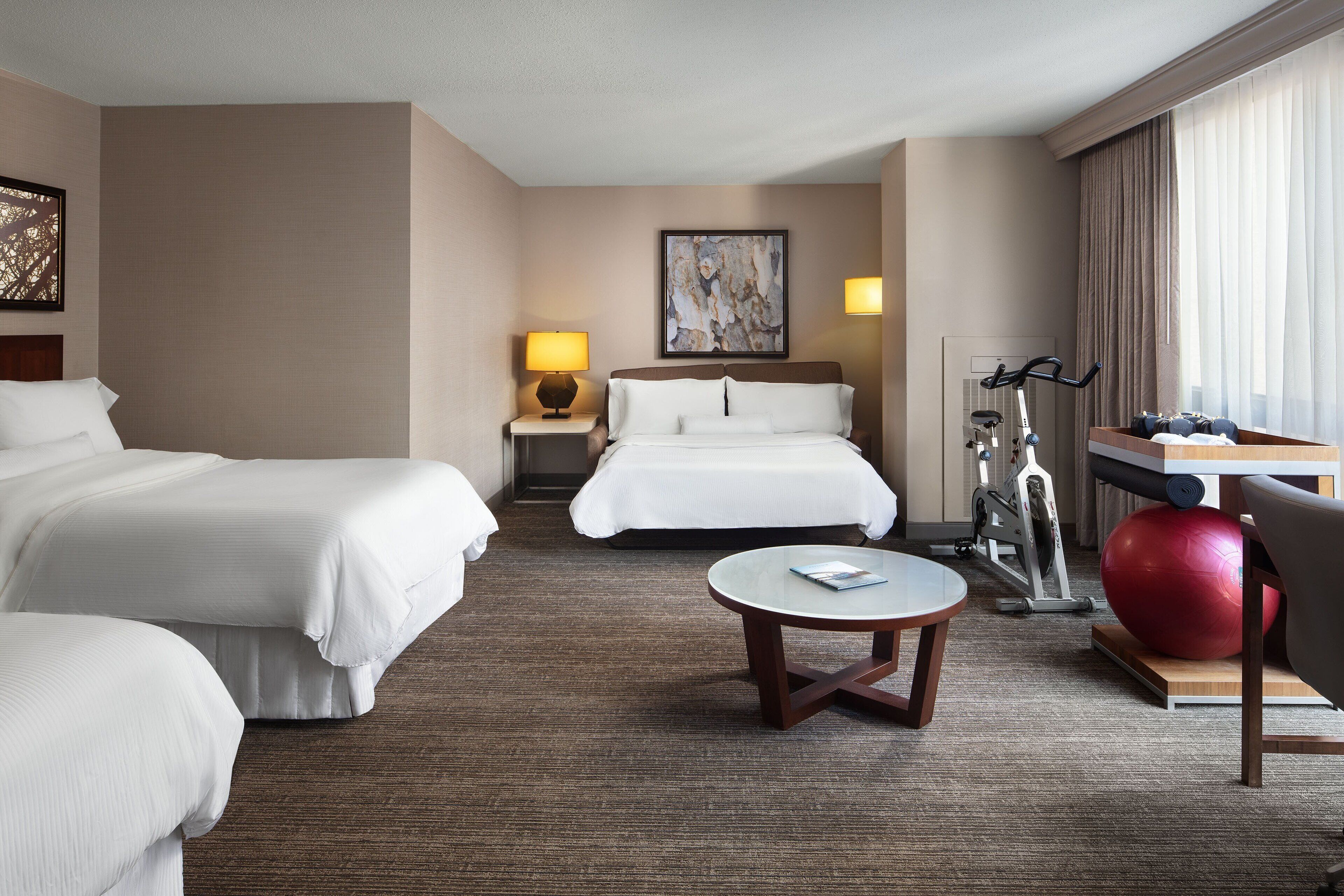 A hotel room with two beds, a small round table, a red exercise ball, and a treadmill.